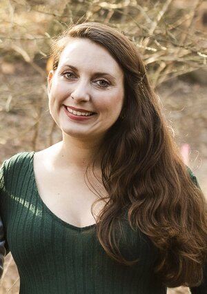 Rebecah is smiling directly at the camera. Her long brown hair is pulled to one side and she is wearing a forest green sweater.